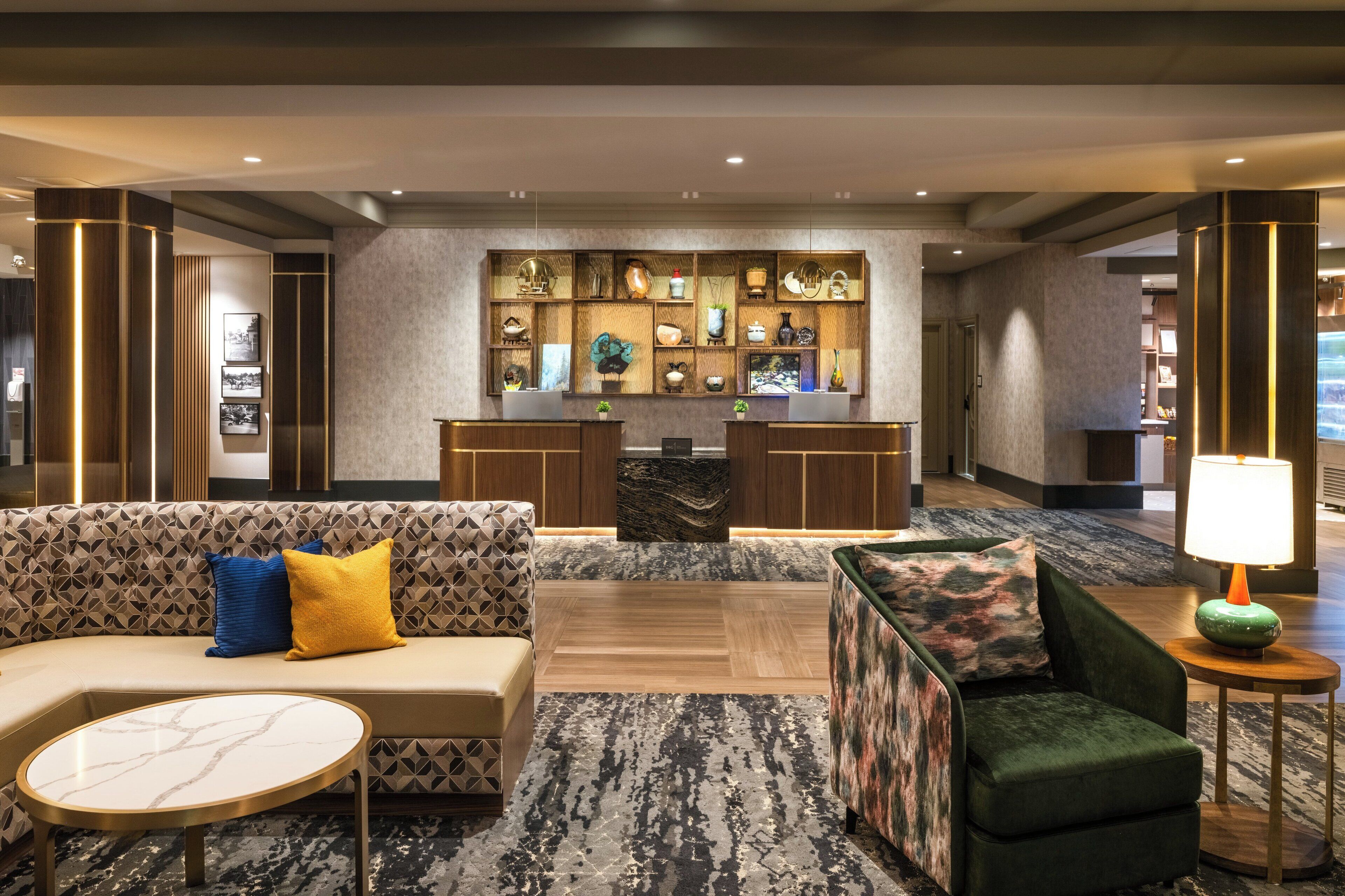 A modern lobby with a sofa, armchairs, a marble coffee table, a reception desk, and a wall display of decorative items.