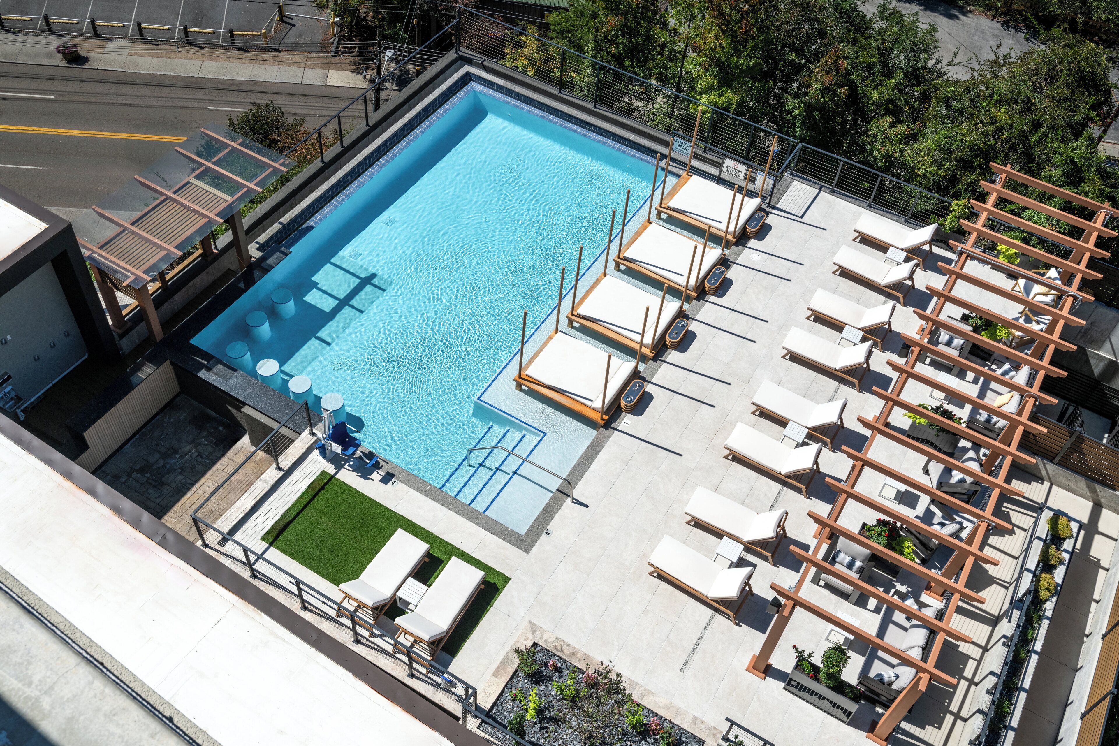 A rooftop swimming pool with sun loungers and a small grassy area.