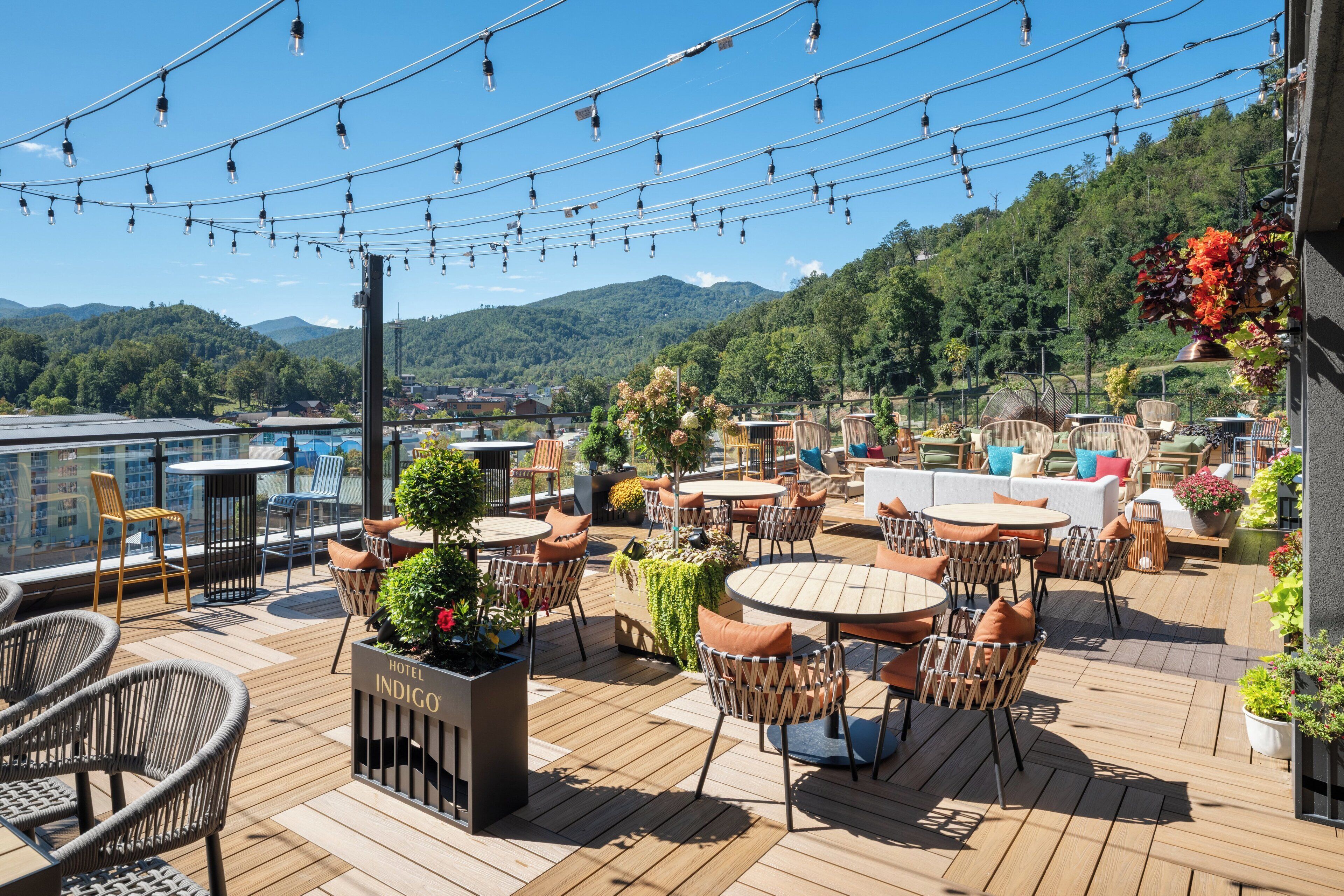 Une terrasse sur le toit dotée de plusieurs espaces aménagés, notamment des tables et des chaises rondes, le tout entouré de plantes et de fleurs en pot.