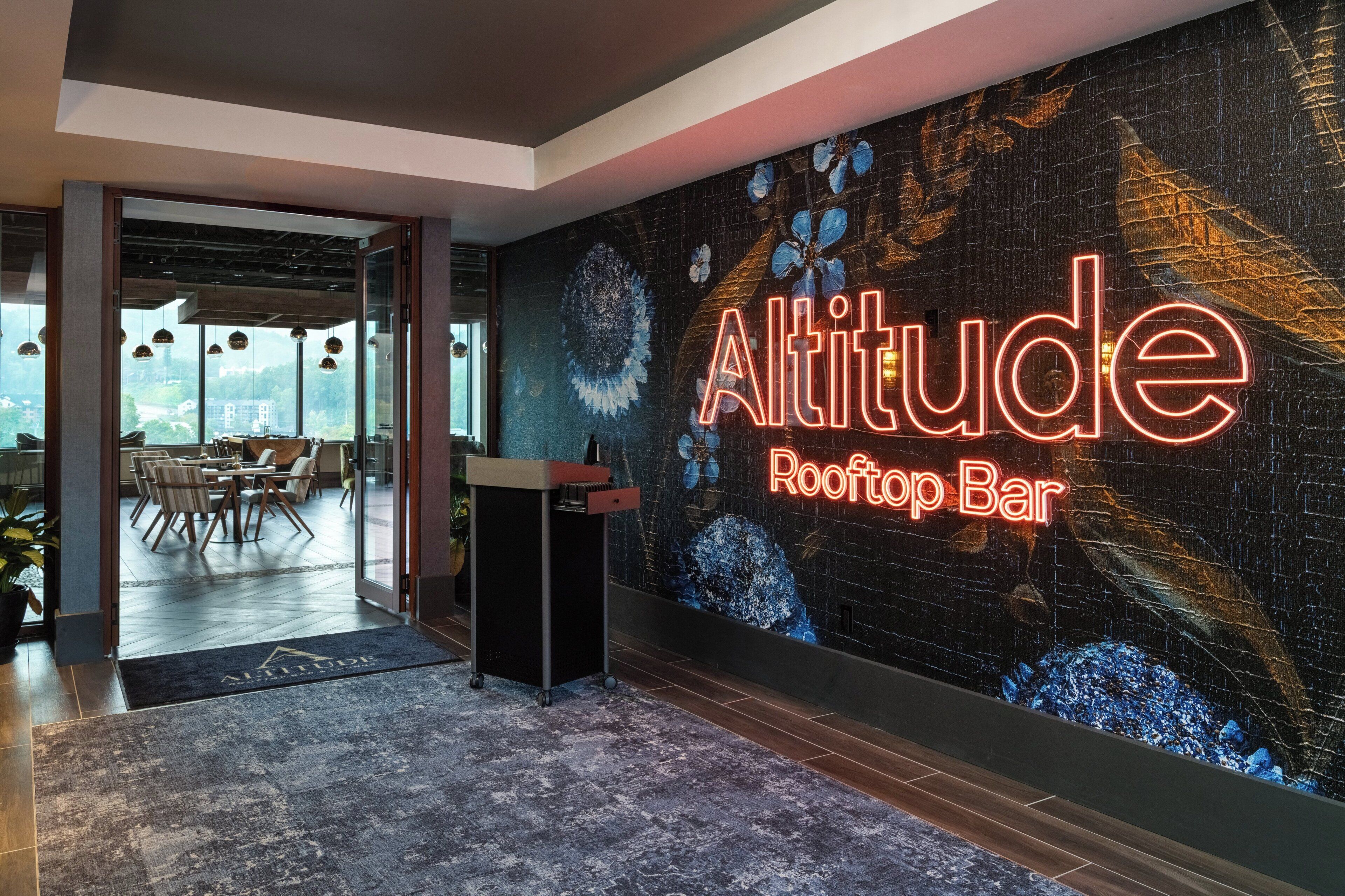 A modern interior with a large wall mural, a reception desk, and a view into a dining area.