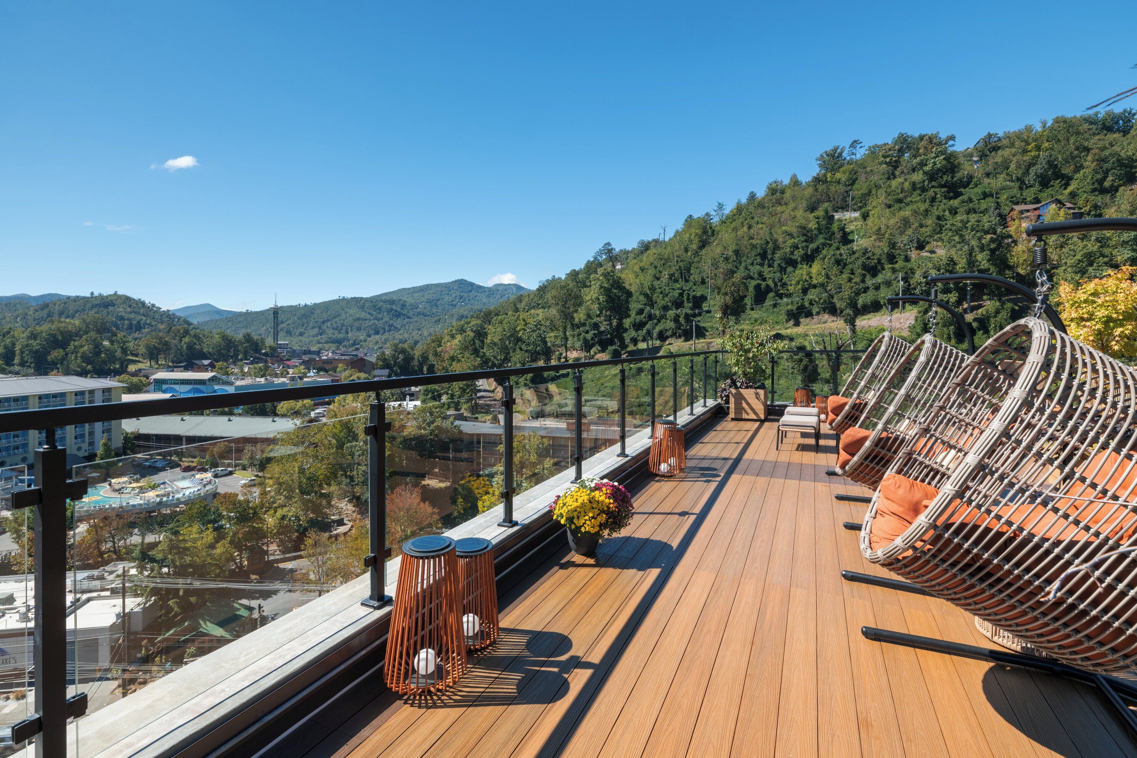 A deck with wicker chairs and a table, overlooking a scenic view of a town and mountains.