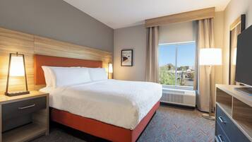 Una habitación de hotel con cama, mesitas de noche, televisor y ventana con cortinas.