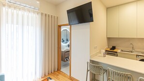 Habitación de hotel moderna con kitchenette, un televisor de pantalla plana sobre la encimera y baño visible a través de una puerta.