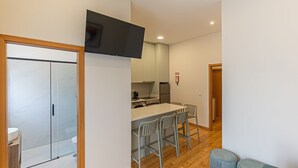Una cocina moderna con comedor, un televisor de pantalla plana sobre la encimera y una pequeña zona de estar con un otoman redondo.