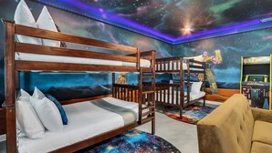 Une chambre avec des lits superposés, une fresque murale sur le thème de l’espace et une console de jeux.