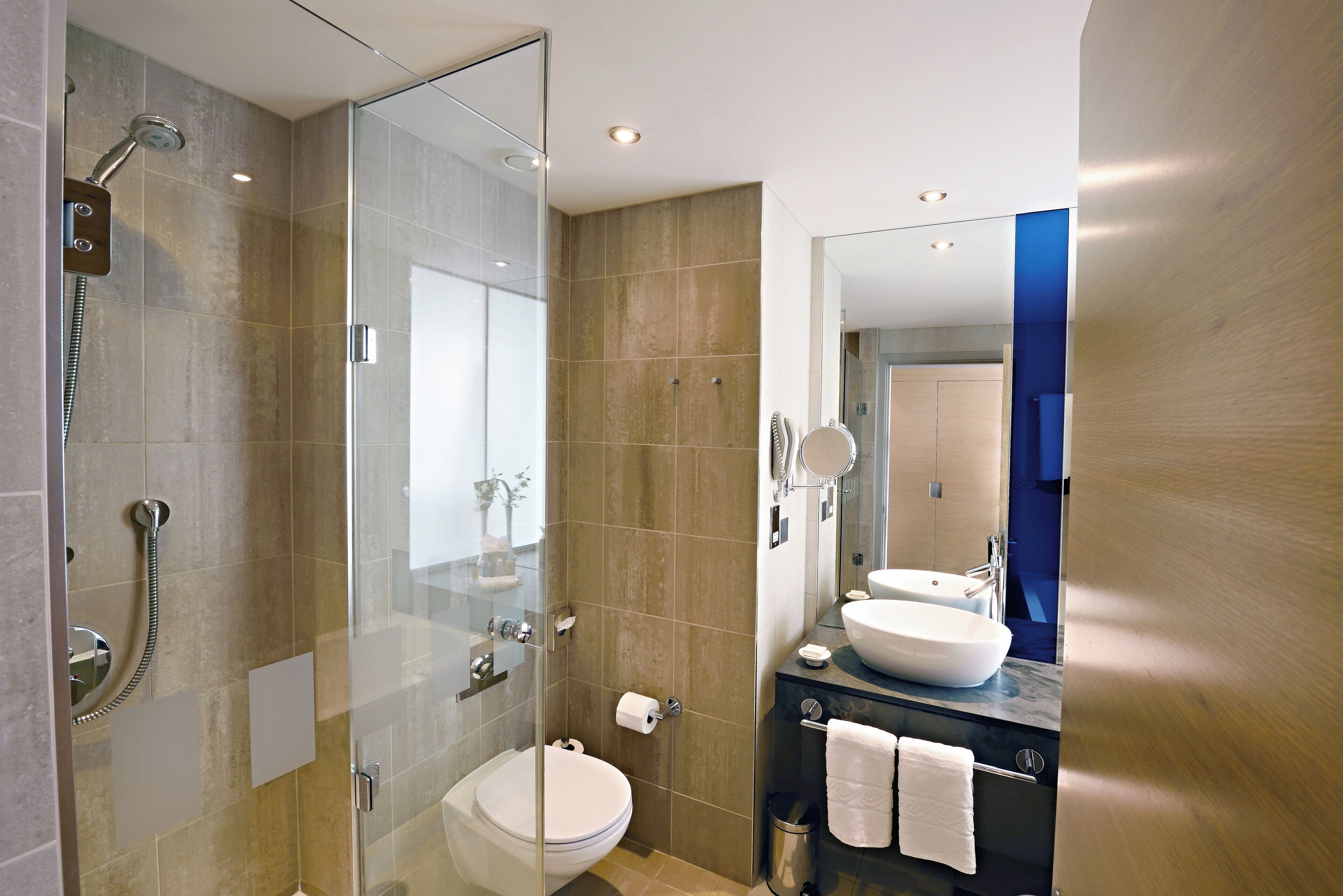 Un baño moderno con ducha de vidrio, inodoro, lavamanos y espejo.