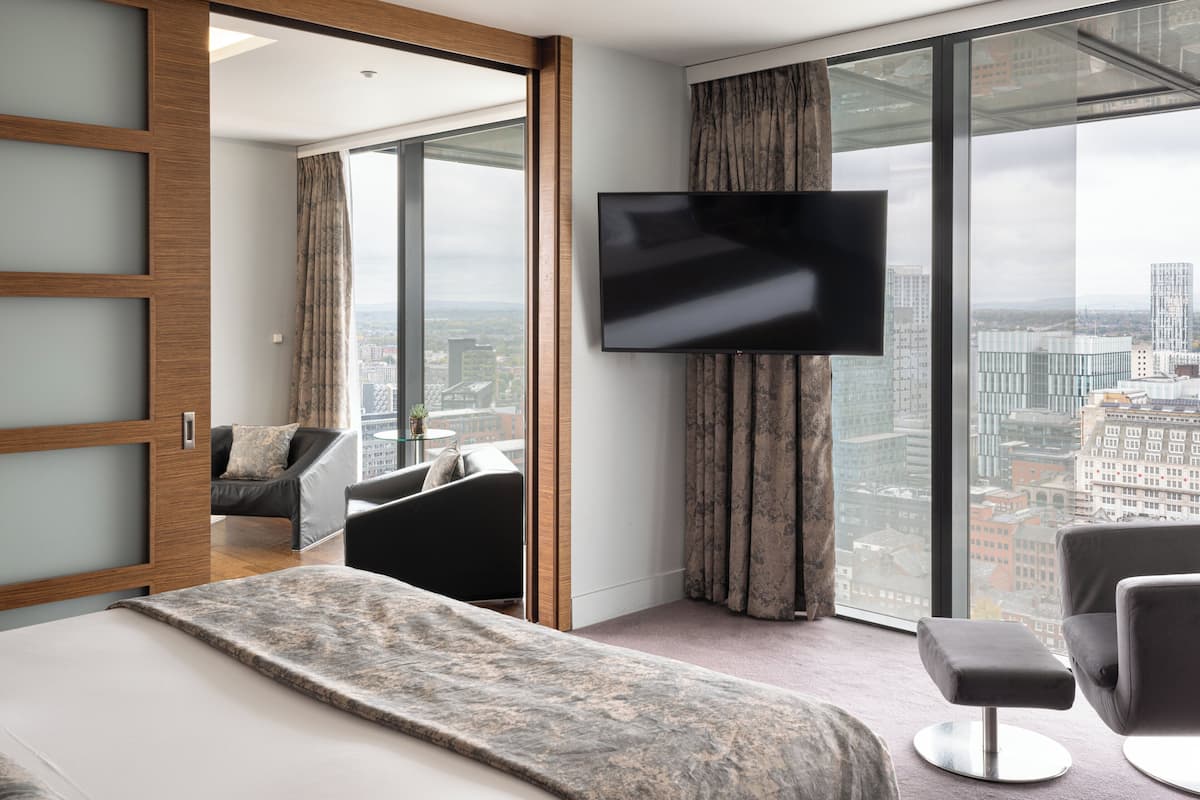 Een moderne hotelkamer met een groot bed, een televisie, een sofa en uitzicht op de stad.