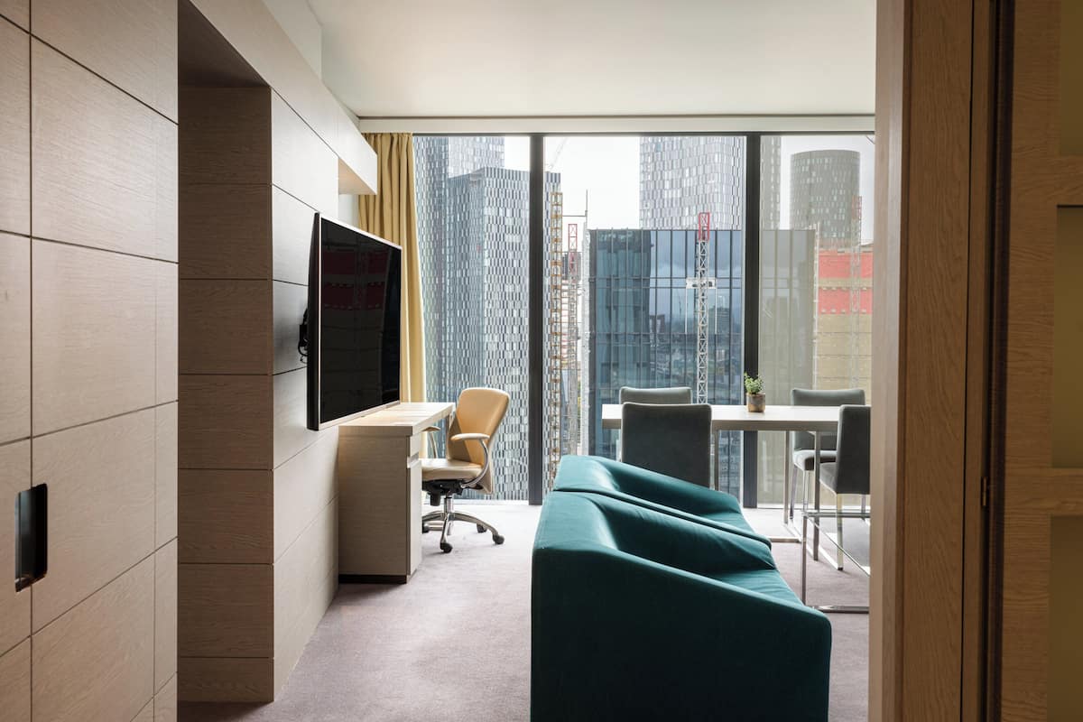 Een hotelkamer met een groot raam, een bureau, een stoel, een bank en een televisie.