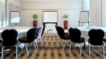 A conference room with a large table, chairs, a projector screen, and potted plants.