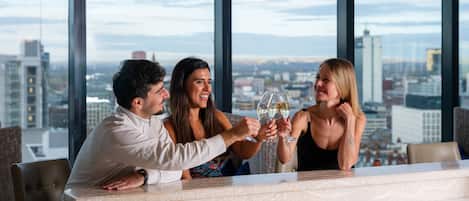 Un bar de hotel de gran altura con vistas a la ciudad, ventanas amplias y un diseño interior moderno.