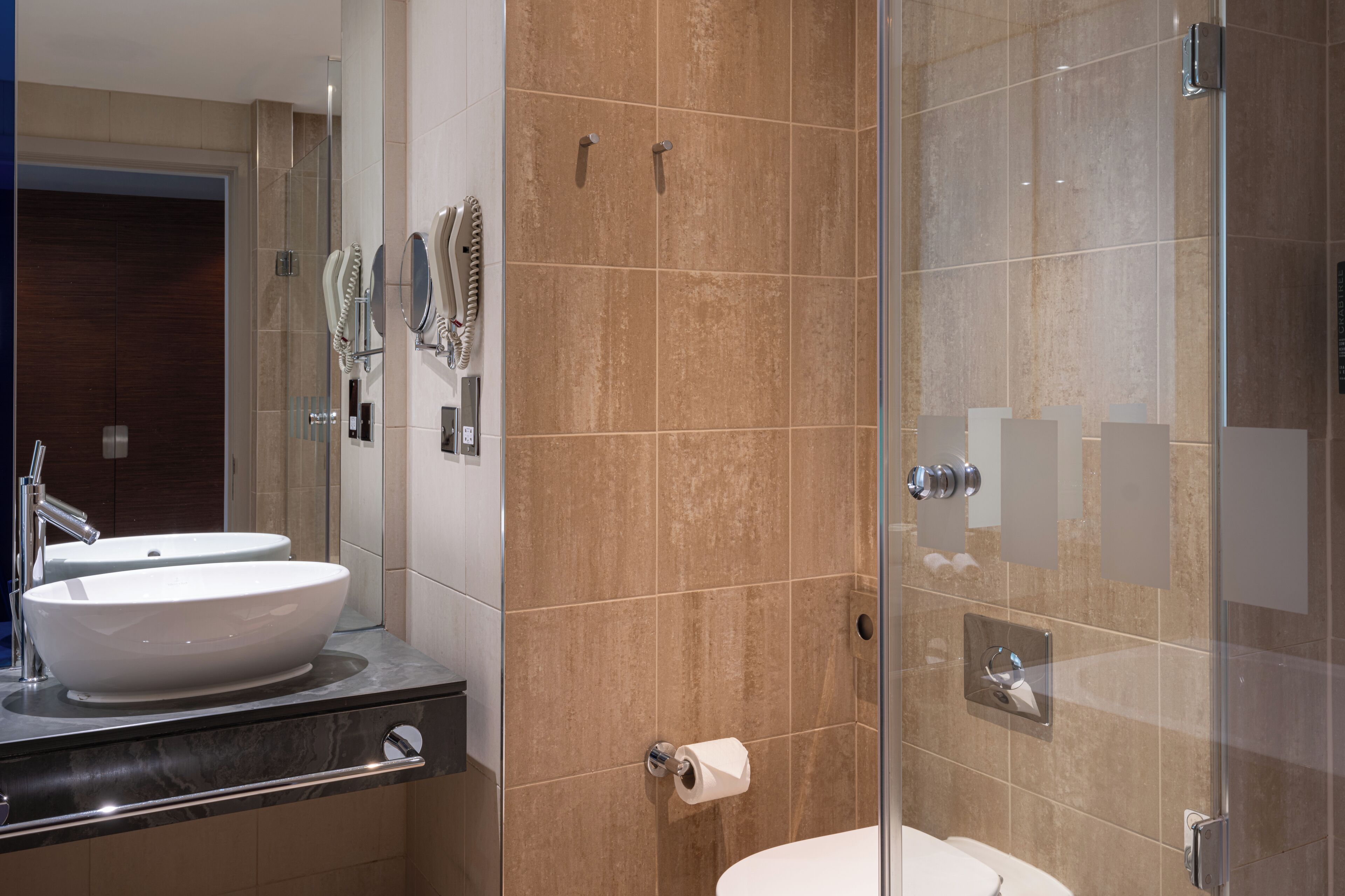 A modern bathroom with a glass shower enclosure, a double sink vanity, and a toilet.