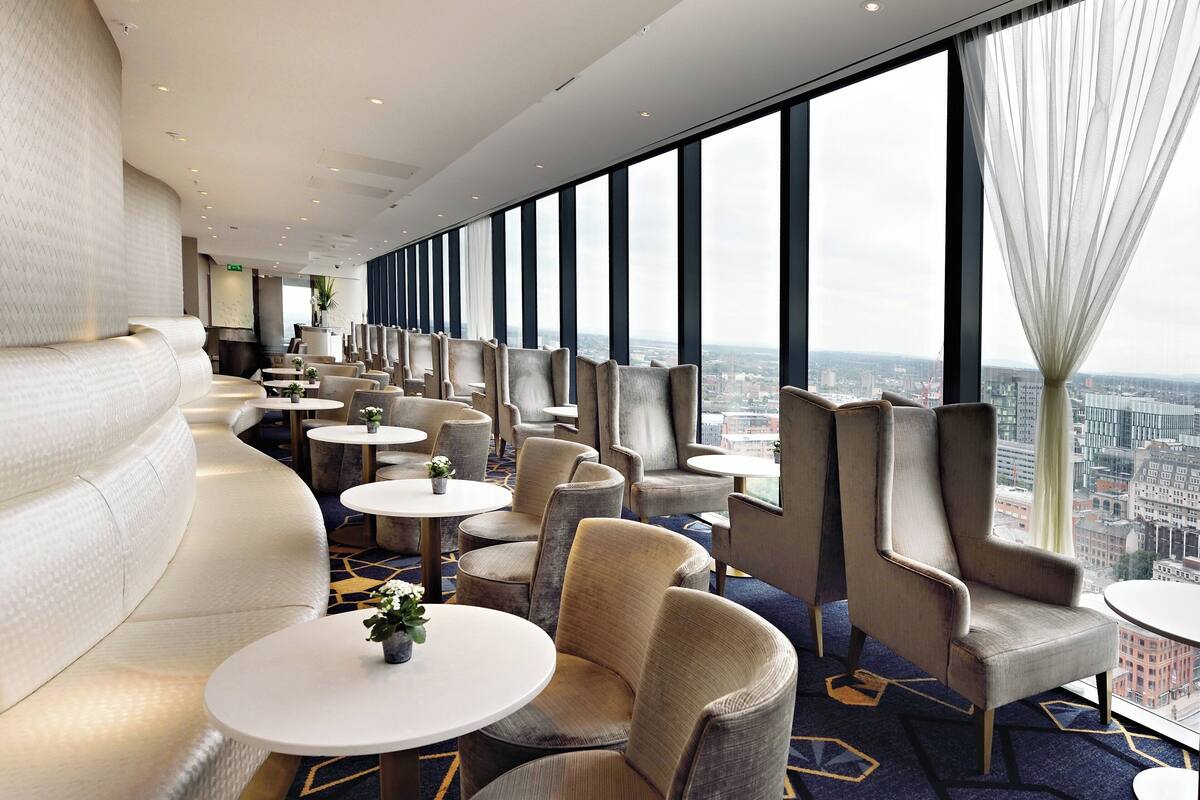 Een moderne hotelentree met een gebogen zithoek, ronde tafels en grote ramen met uitzicht over de stad.