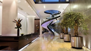A modern lobby with a curved staircase, large potted plants, and a polished floor. - The Manchester Deansgate Hotel by IHG (Manchester)