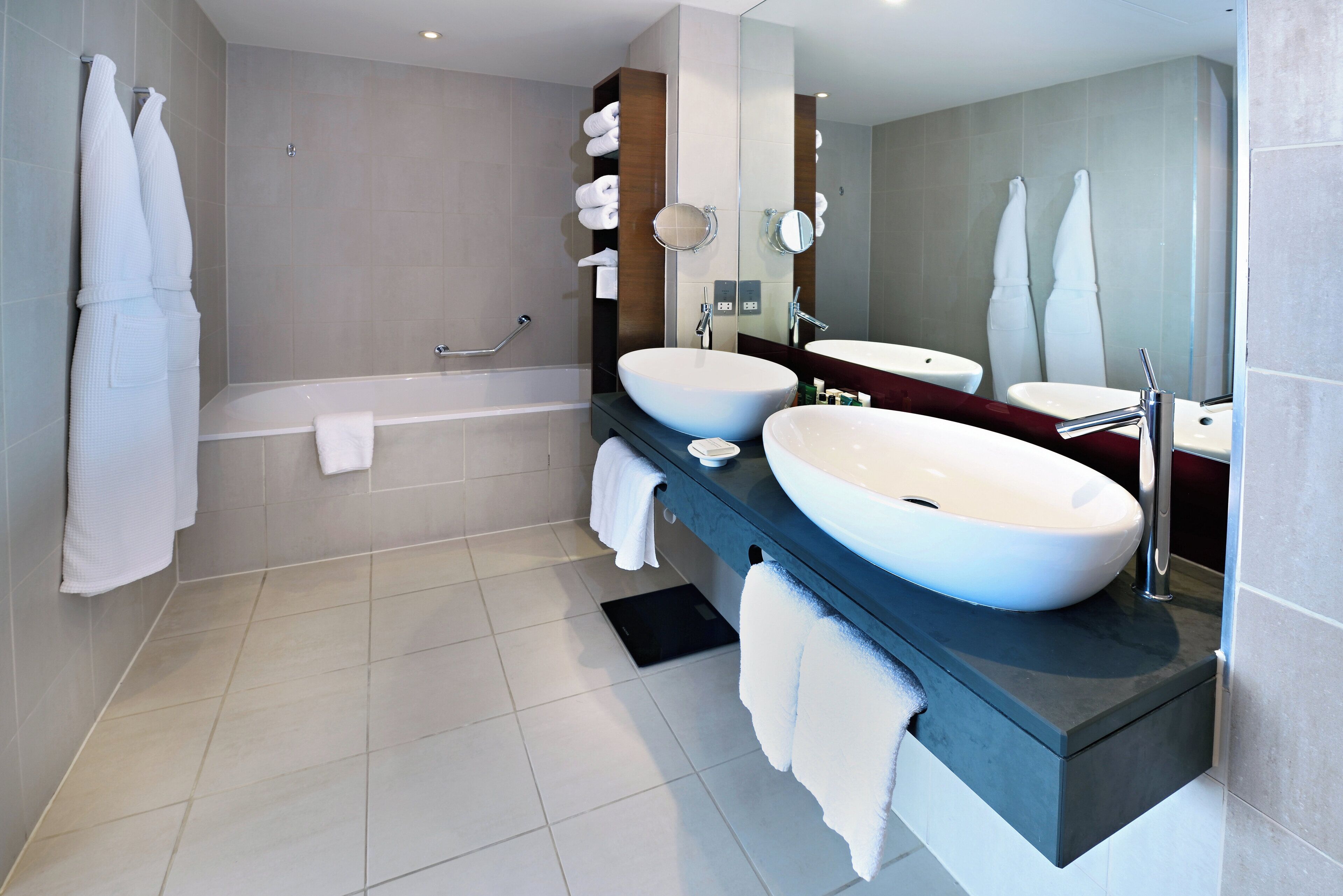 Une salle de bain moderne avec deux lavabos, une baignoire et un grand miroir.