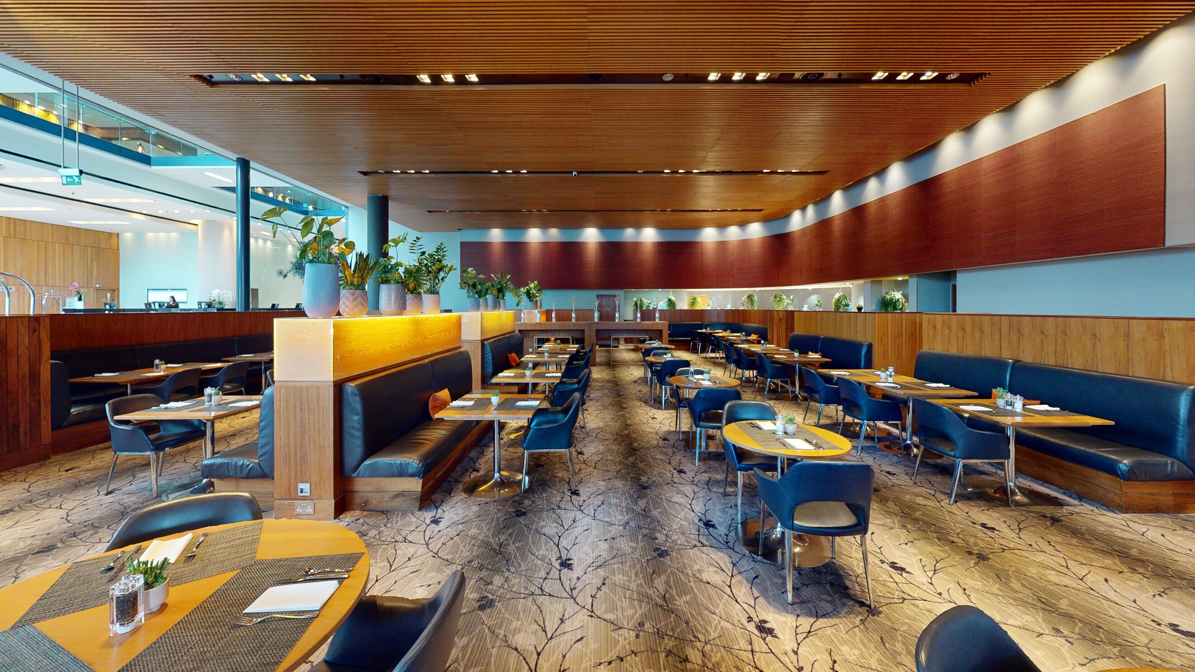 Un restaurante moderno con cabinas y mesas, techo de madera y plantas en macetas.