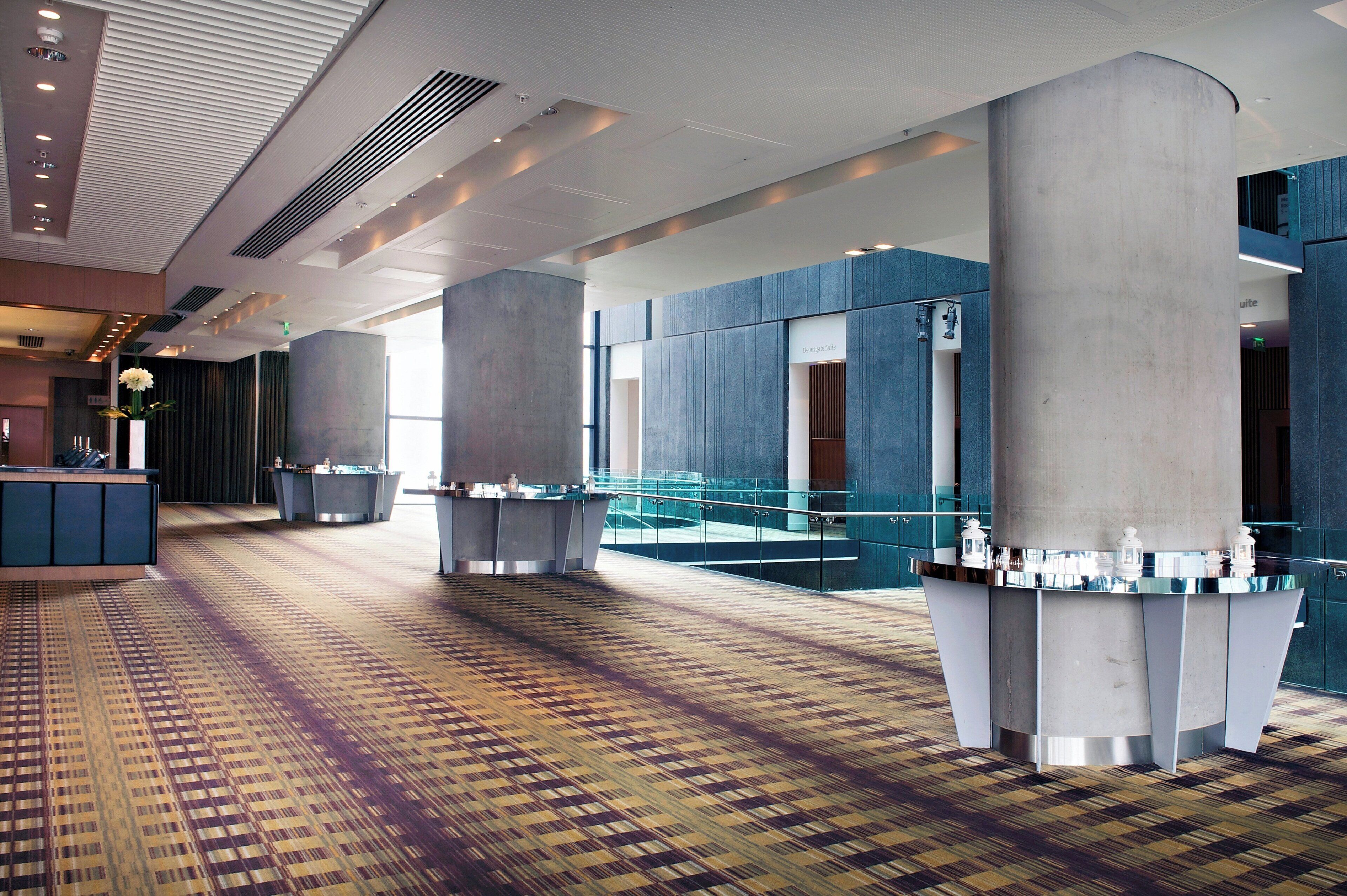 A spacious lobby with a patterned carpet, large pillars, and a glass railing overlooking a lower level.
