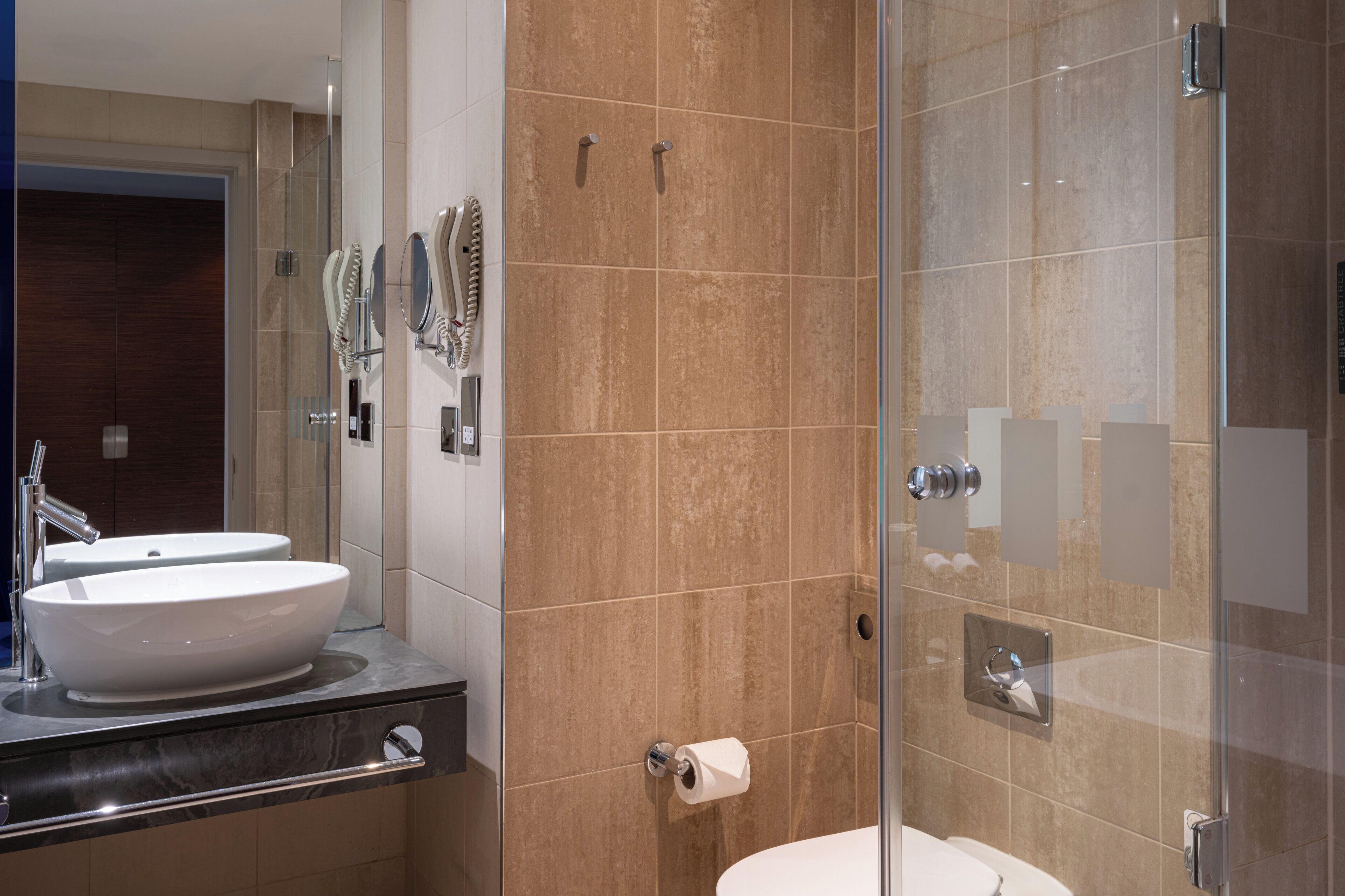 Un baño moderno con un espejo grande, dos lavamanos, cabina de ducha con paredes de vidrio y un inodoro.