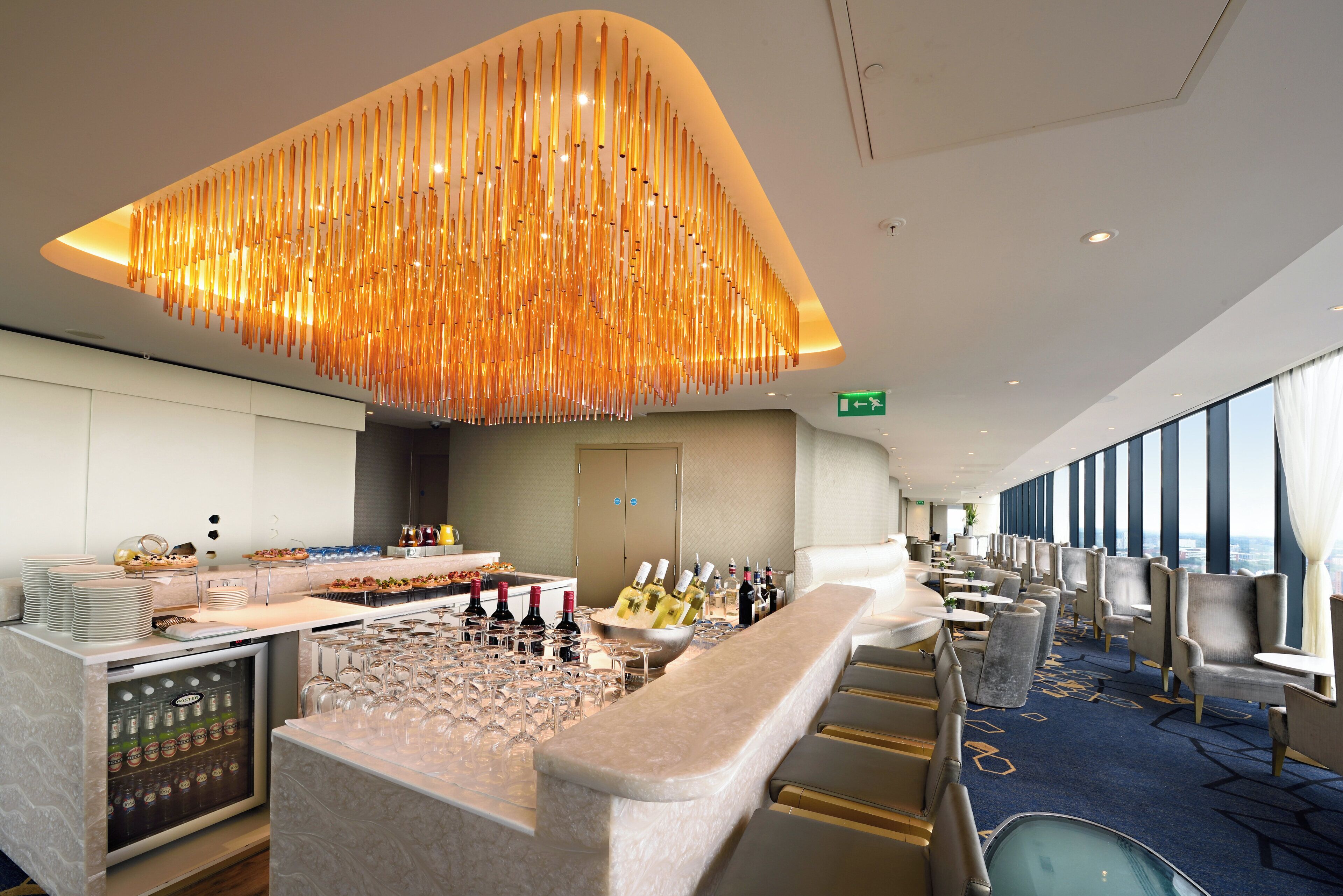 Un hall d’hôtel comprenant un bar, des espaces pour s’asseoir et une vue dégagée grâce à de grandes fenêtres.