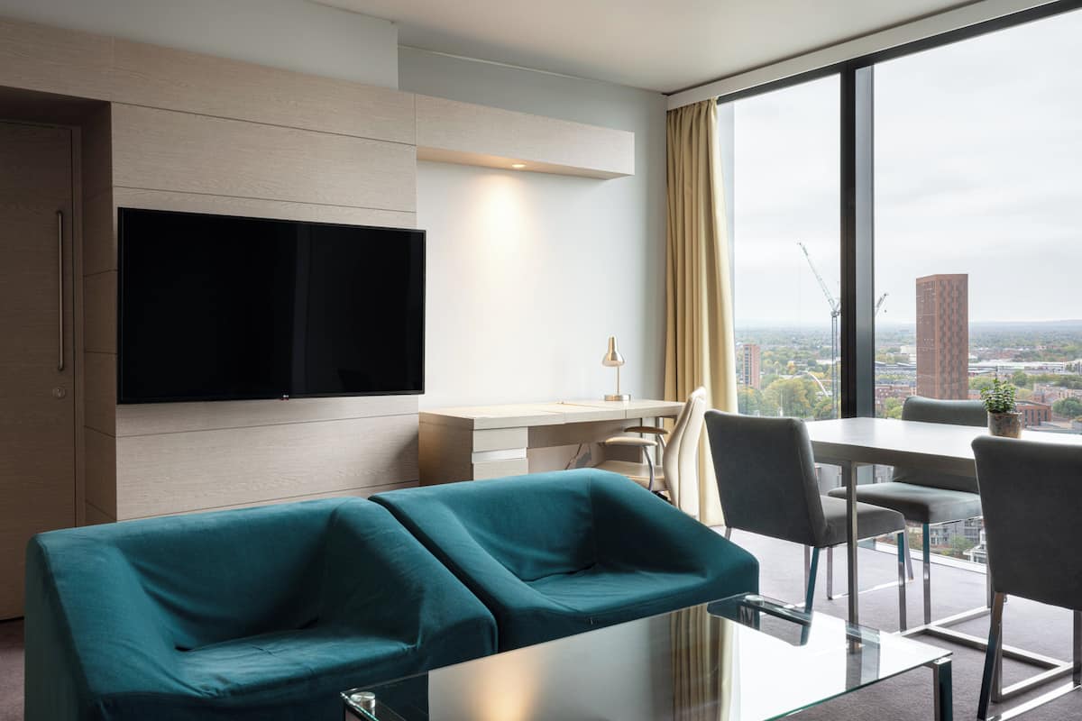 Une chambre d’hôtel moderne dotée d’une grande fenêtre, d’un téléviseur à écran plat, d’un coin repas et d’un canapé.