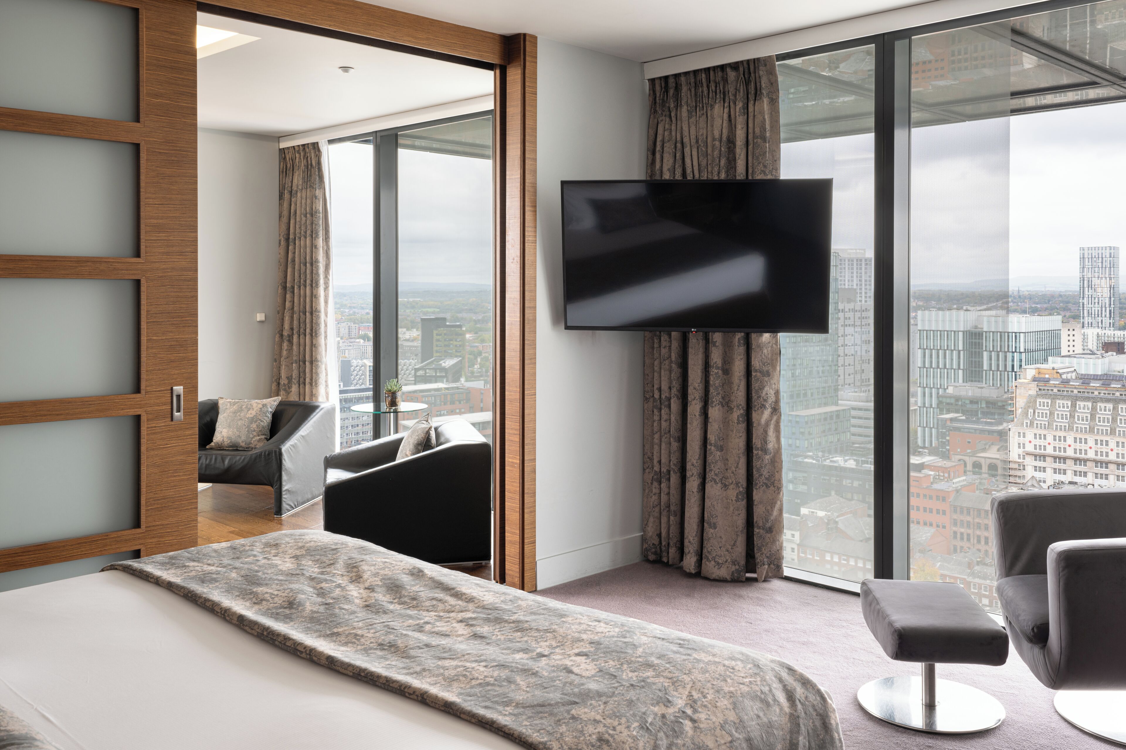 Une chambre d’hôtel moderne dotée d’un grand lit, d’un téléviseur à écran plat, d’une vue sur la ville et d’une porte-fenêtre coulissante donnant sur un balcon.