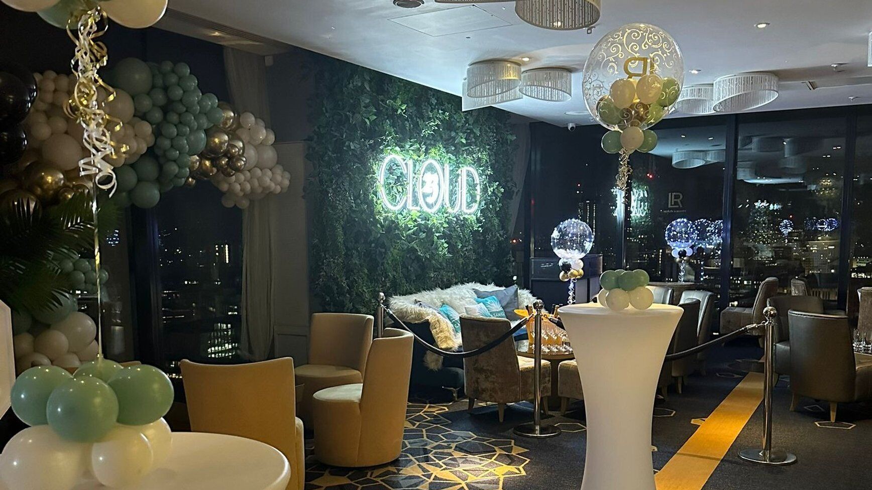 Een hotel lobby met een neonreclame, een zithoek en uitzicht op de skyline.