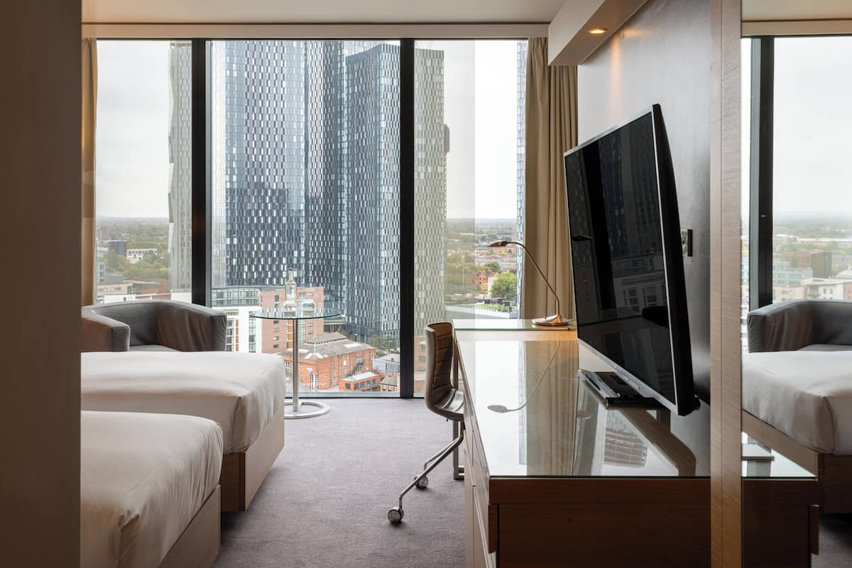 Een hotelkamer met een groot raam, een flatscreen televisie, twee bedden en een bureau.