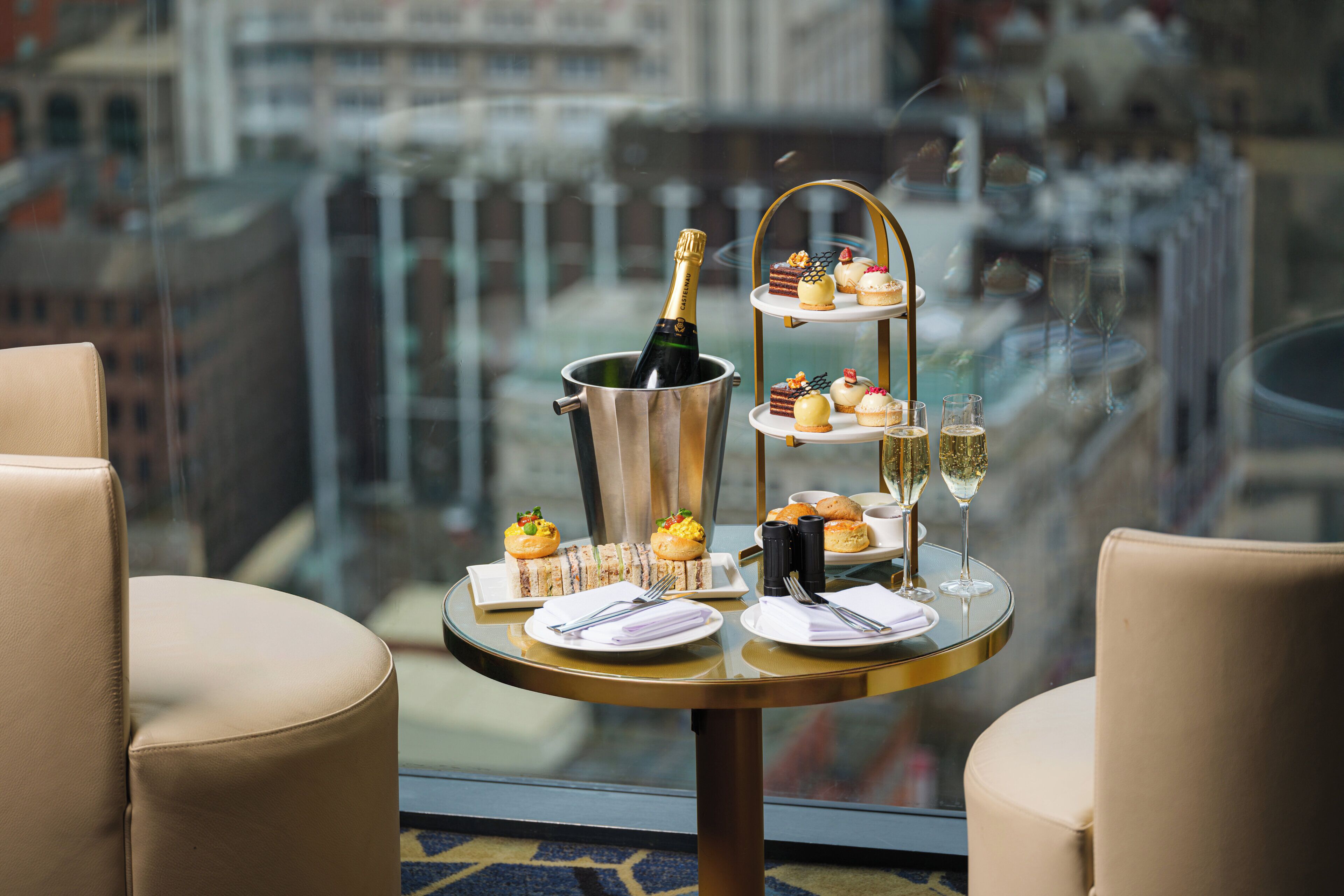 Een tafel met een champagnefles, een etagère met desserts en een glas champagne.