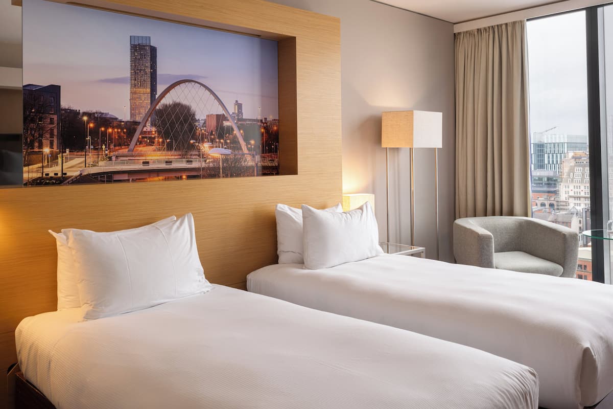 Une chambre d’hôtel avec deux lits, une vue sur la ville, une lampe et une chaise.