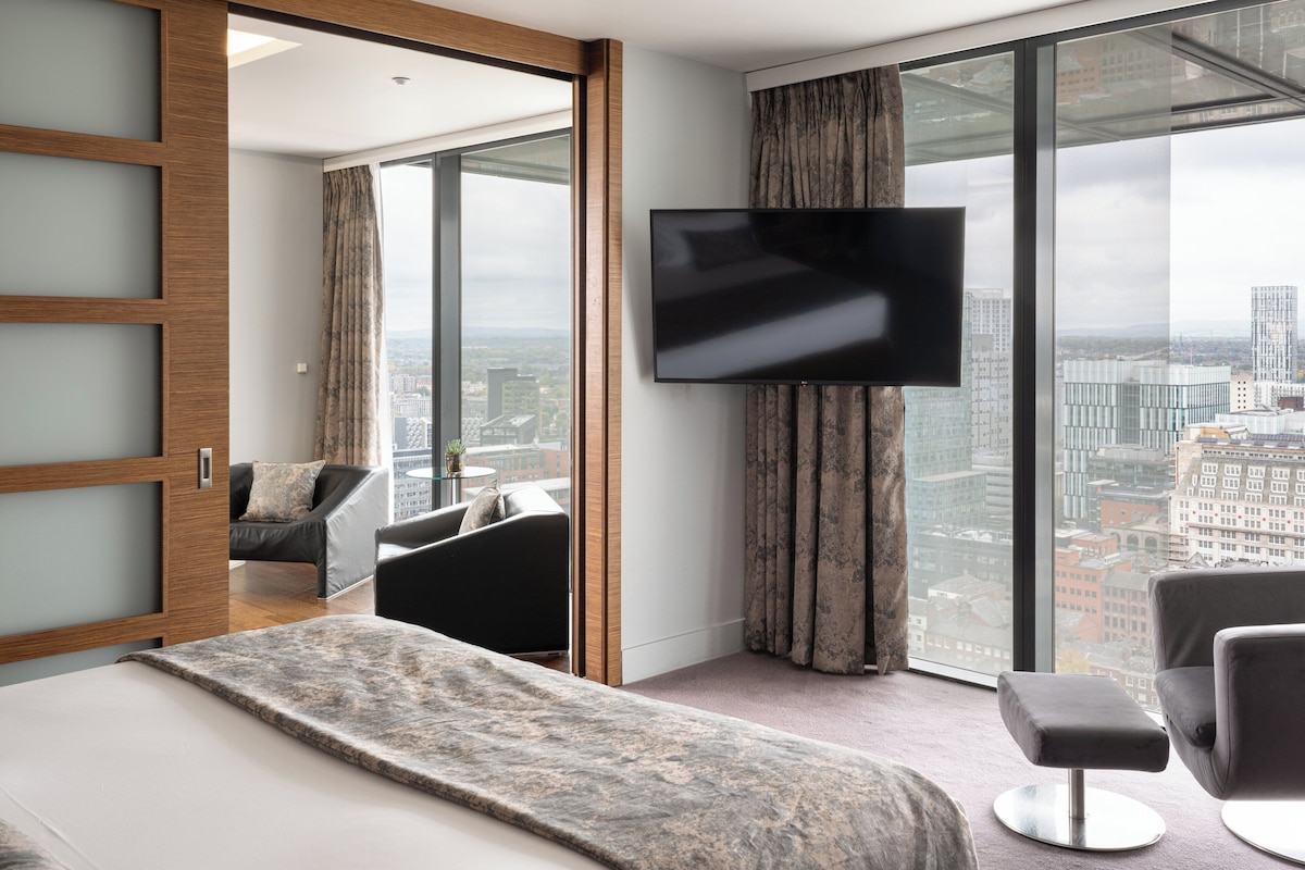 Een moderne hotelkamer met een groot bed, een televisie, een sofa en uitzicht op de stad.