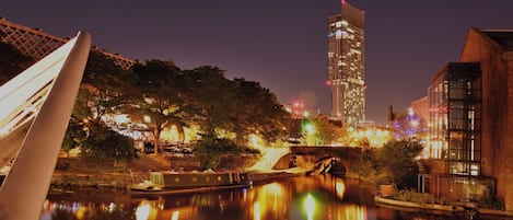 A nighttime cityscape with a river reflecting lights, a modern building, and a bridge.