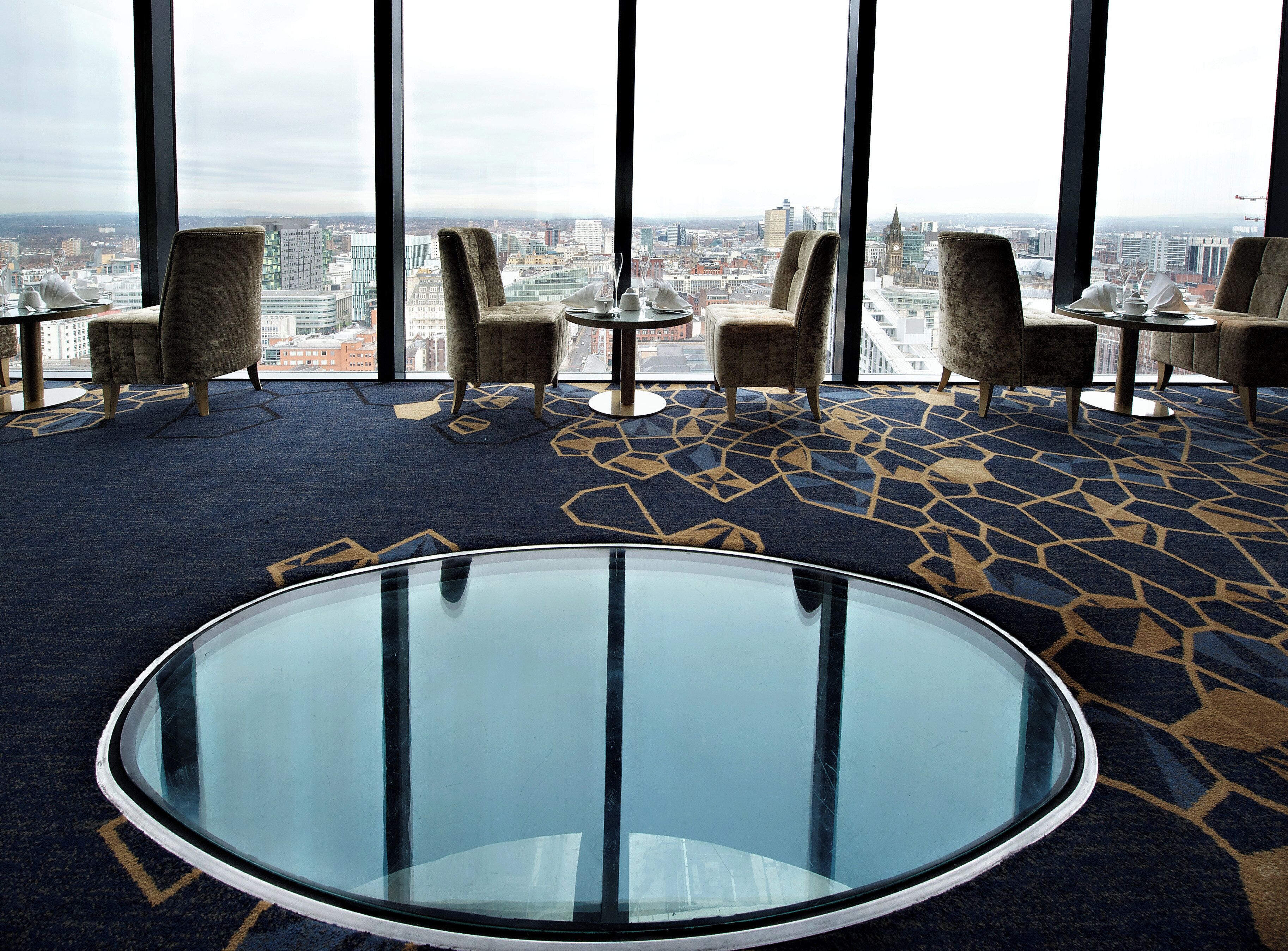 Habitación de hotel moderna con vista panorámica de la ciudad, una mesa redonda de vidrio y asientos cómodos.