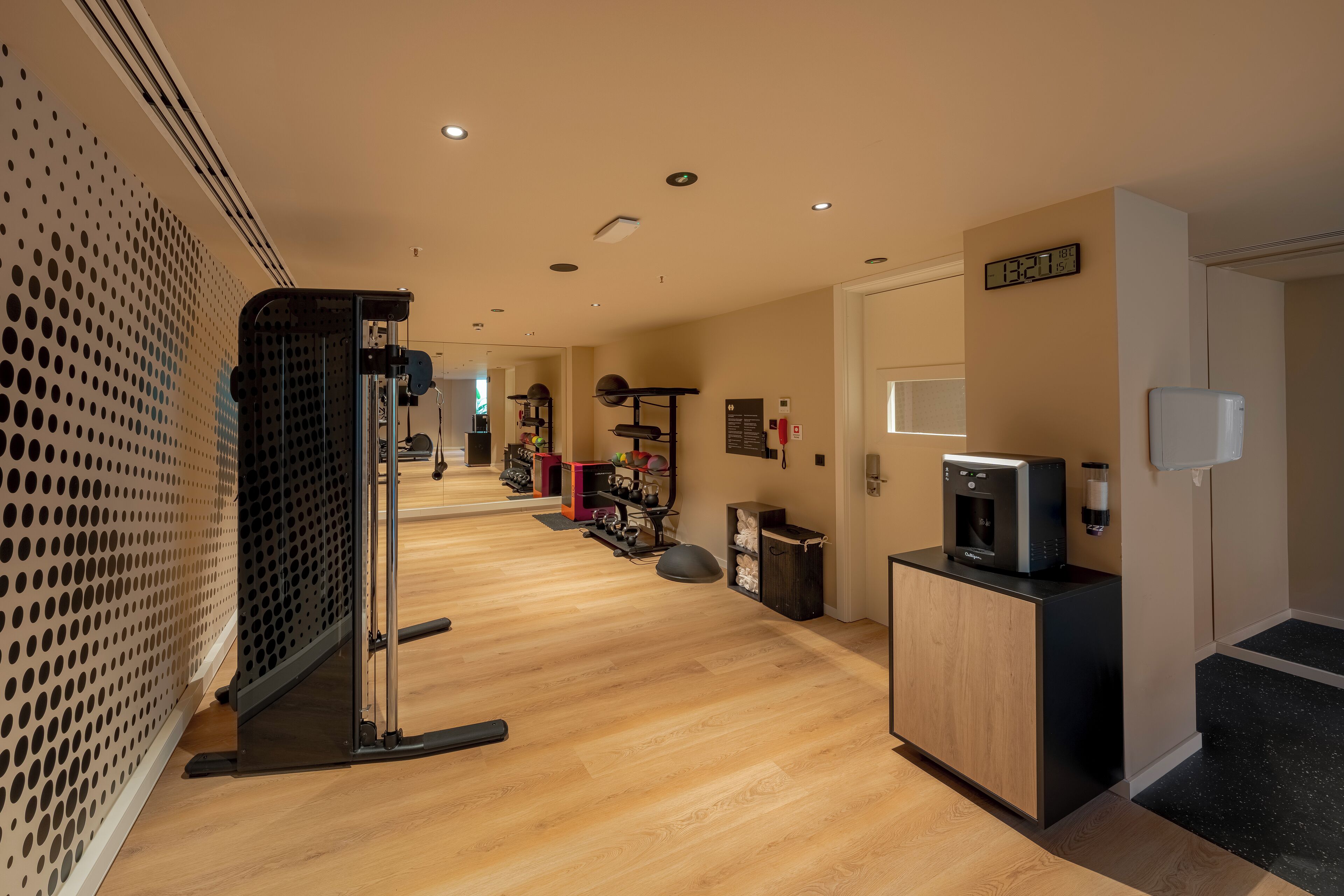 Habitación de hotel con piso de madera, kitchenette, microondas, refrigerador pequeño y puerta con reloj digital.