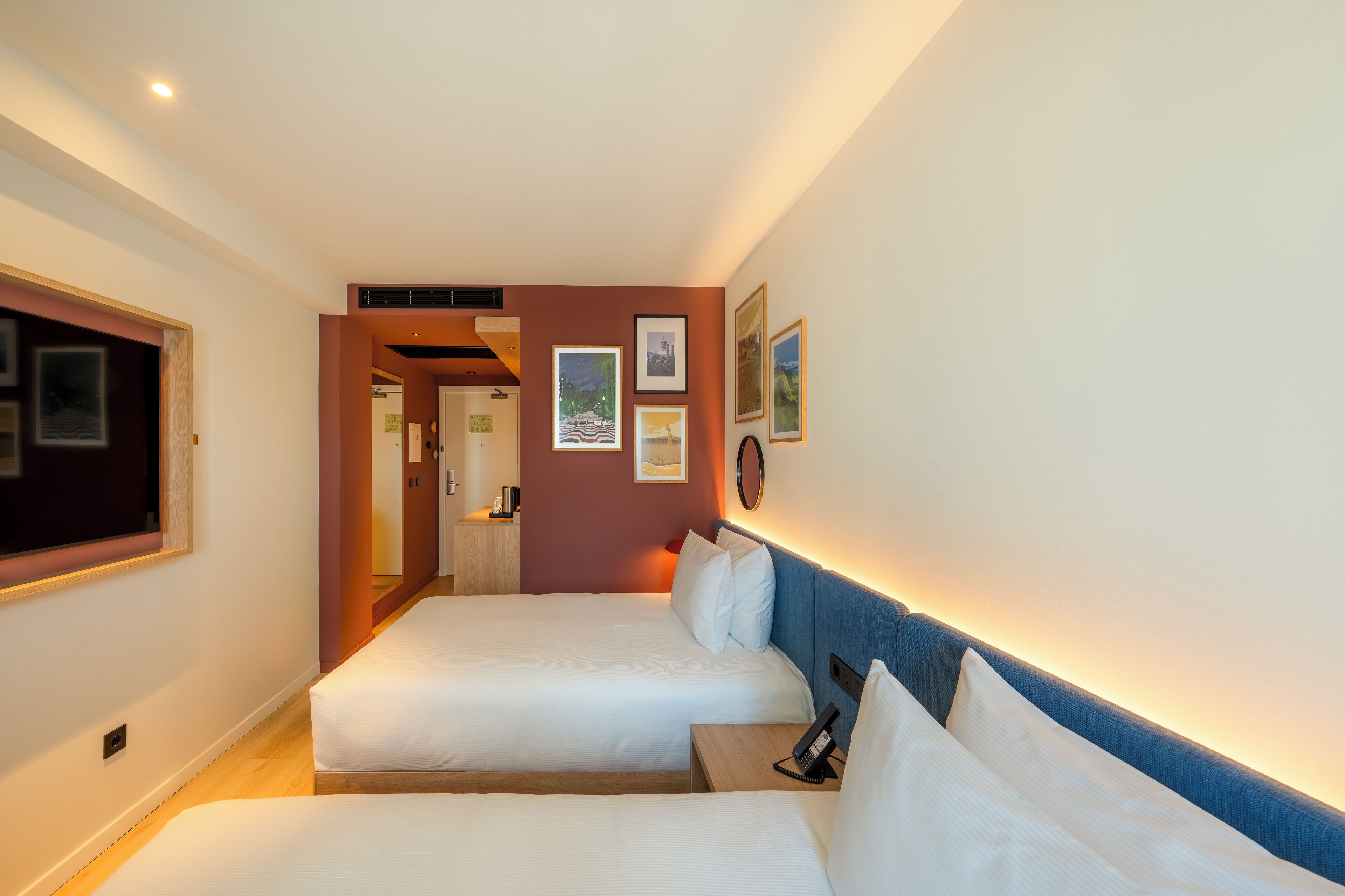 Een hotelkamer met twee bedden, een nachtkastje met een telefoon, en wanddecoratie met foto's.