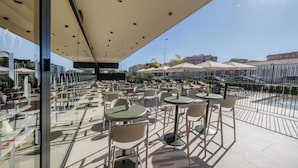An outdoor seating area with tables and chairs, a glass partition, and umbrellas. - Hampton By Hilton Alicante Airport (Elche)
