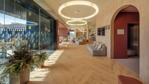 A spacious lobby with a wooden floor, a seating area with sofas, and a large glass wall offering a view of the city. - Hampton By Hilton Alicante Airport (Elche)