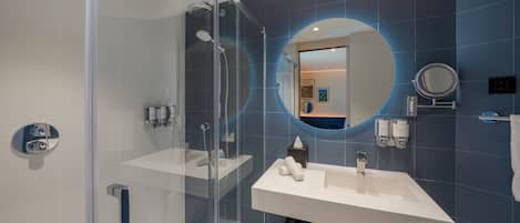 A modern bathroom with a glass-enclosed shower, a white sink, and a large mirror.