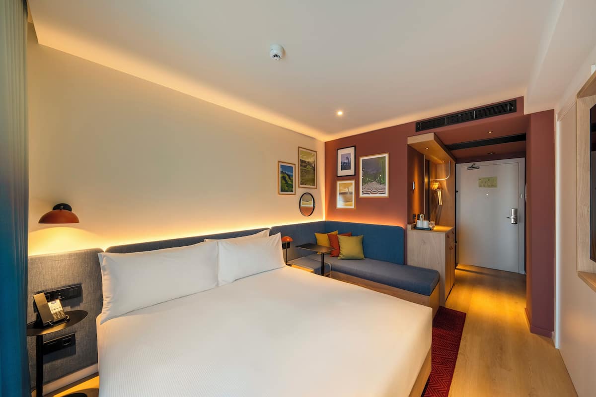 Quarto de hotel com uma cama grande, um sofá, uma escrivaninha e uma porta que dá para um banheiro.
