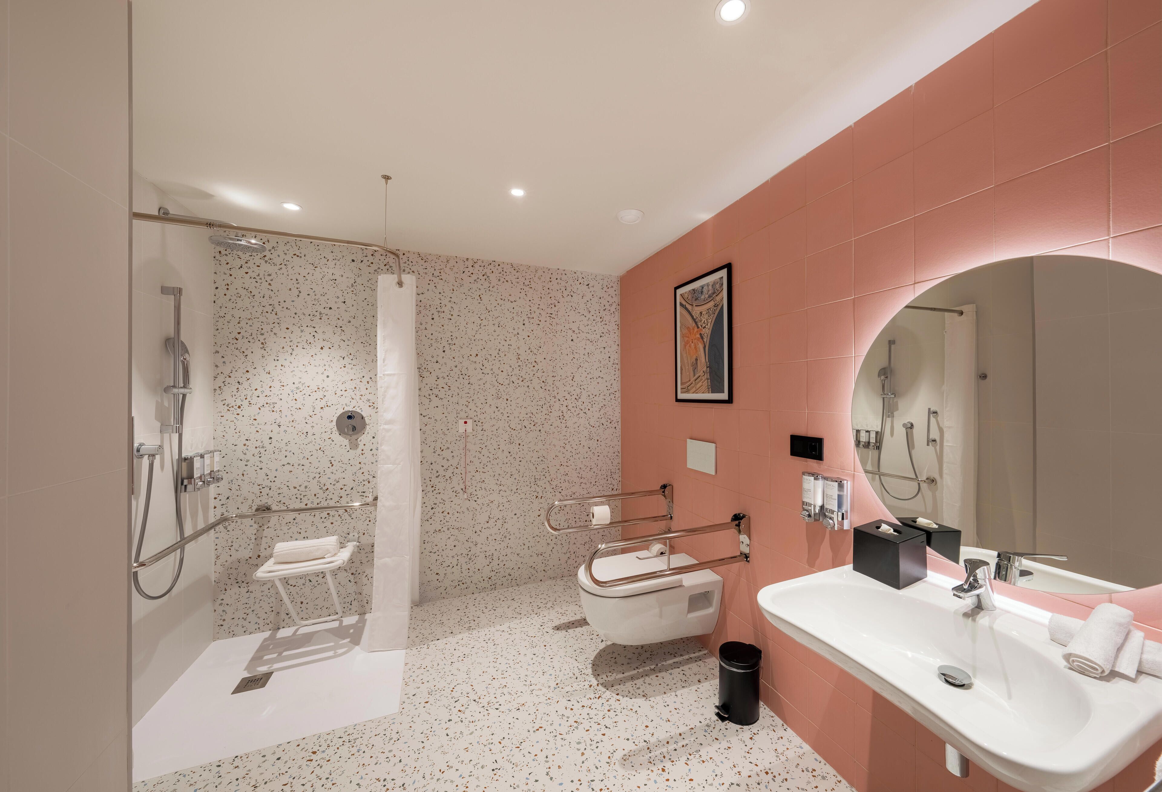 Een moderne badkamer met douche, toilet en wastafel, met een spikkeltjes vloer en roze wanden.