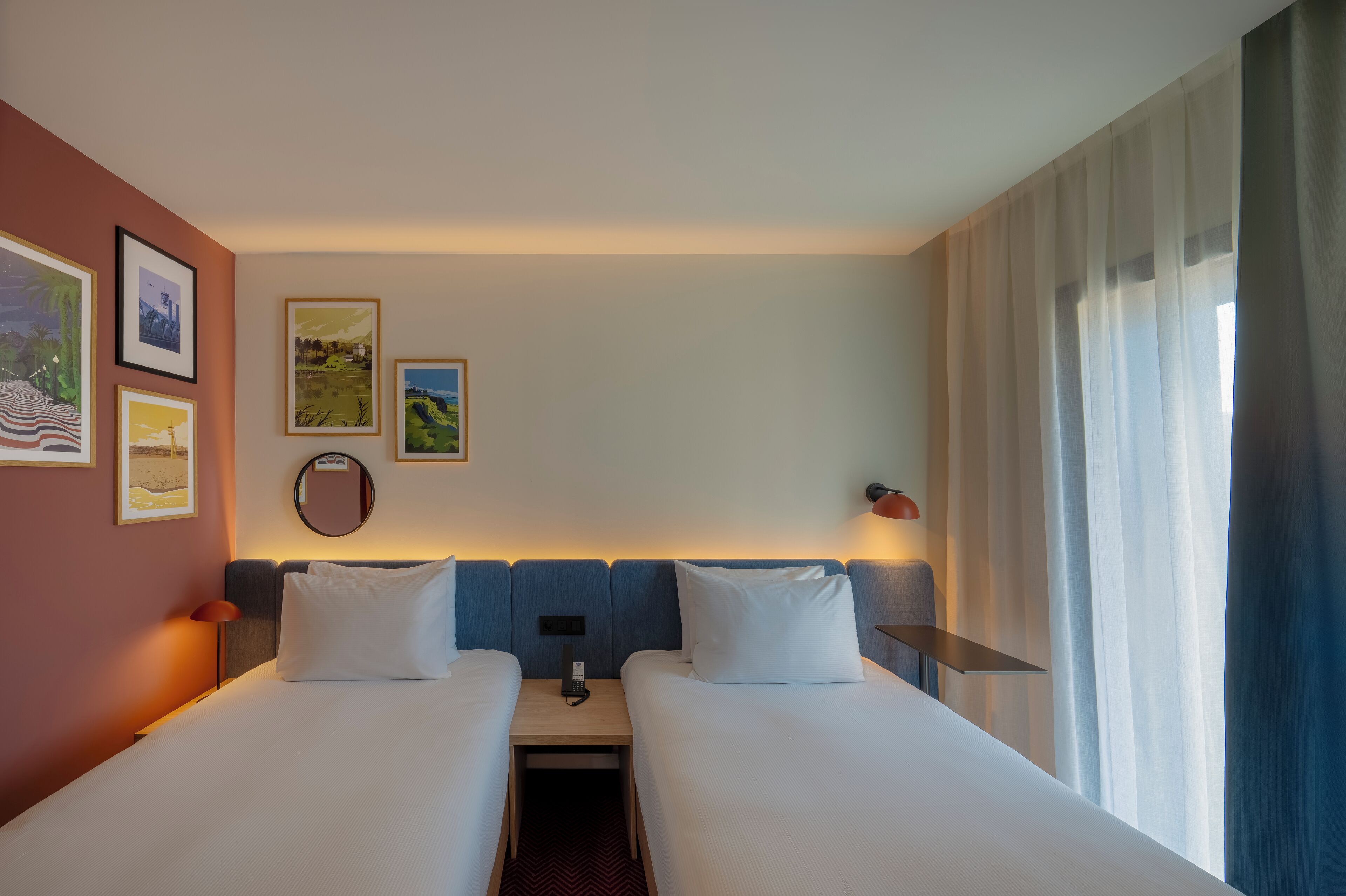 Een hotelkamer met twee bedden, een nachtkastje, een lamp en kunst aan de muur.