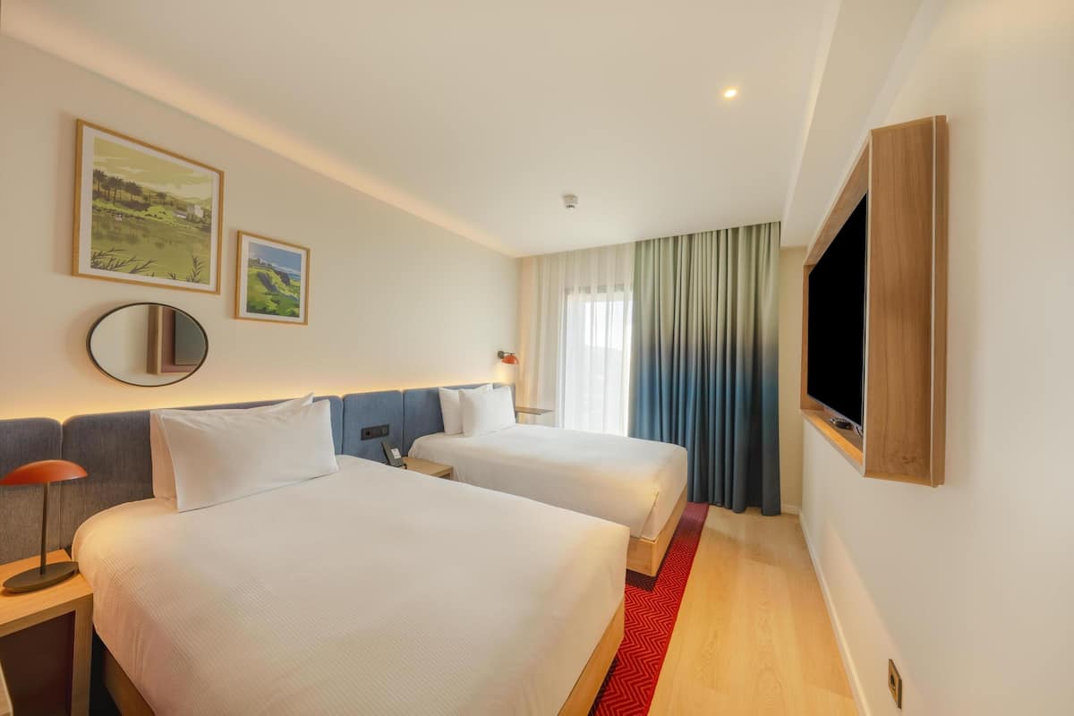 Quarto de hotel com duas camas, televisão, espelho e obras de arte na parede.