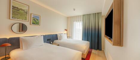 Quarto de hotel com duas camas, televisão, espelho e obras de arte na parede.