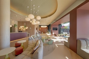 A modern lounge area with a reception desk, seating arrangements, and a dining area. - Hampton By Hilton Alicante Airport (Elche)