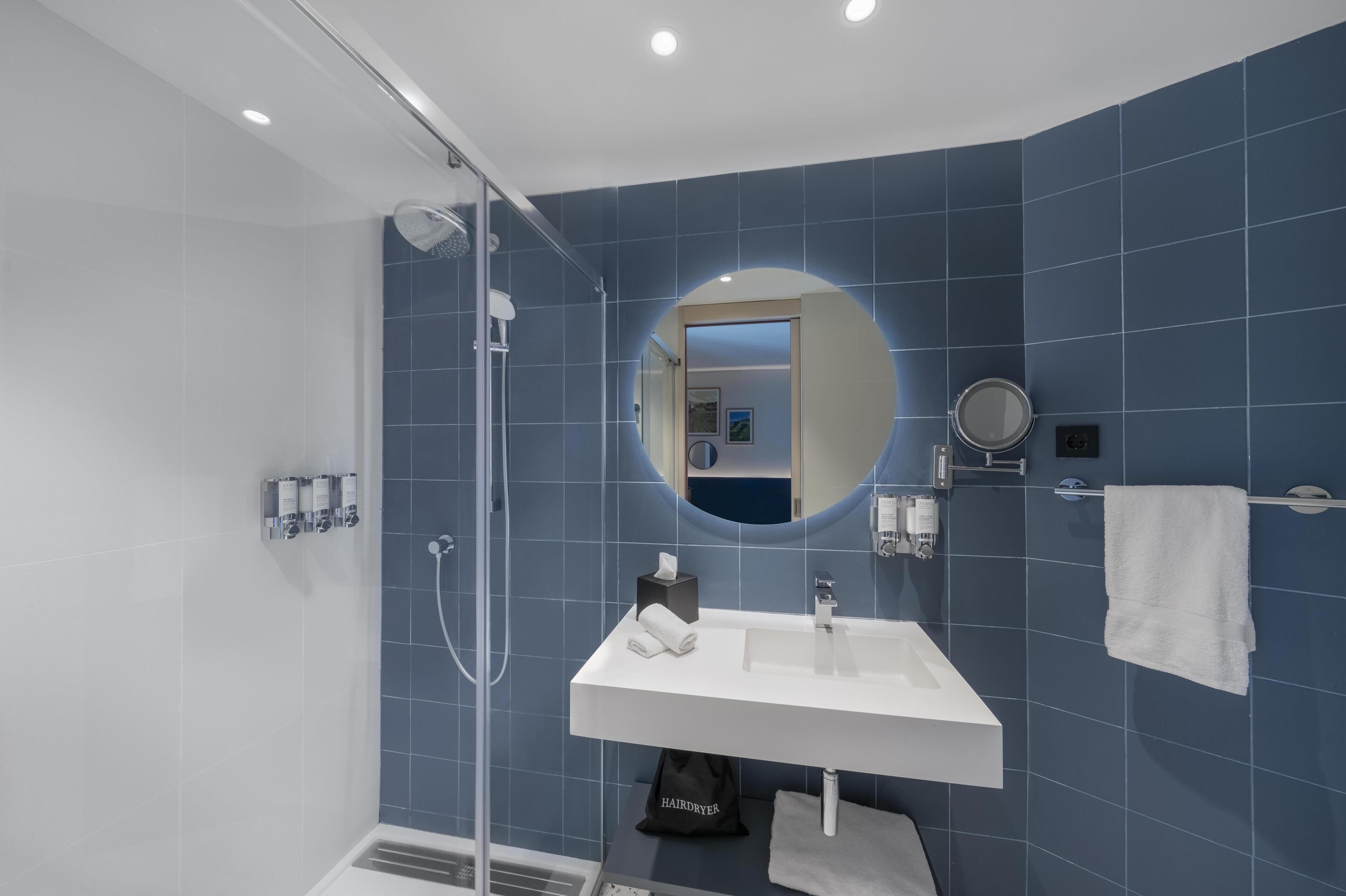 Un baño moderno con cabina de ducha de vidrio, un lavabo blanco y un espejo grande.