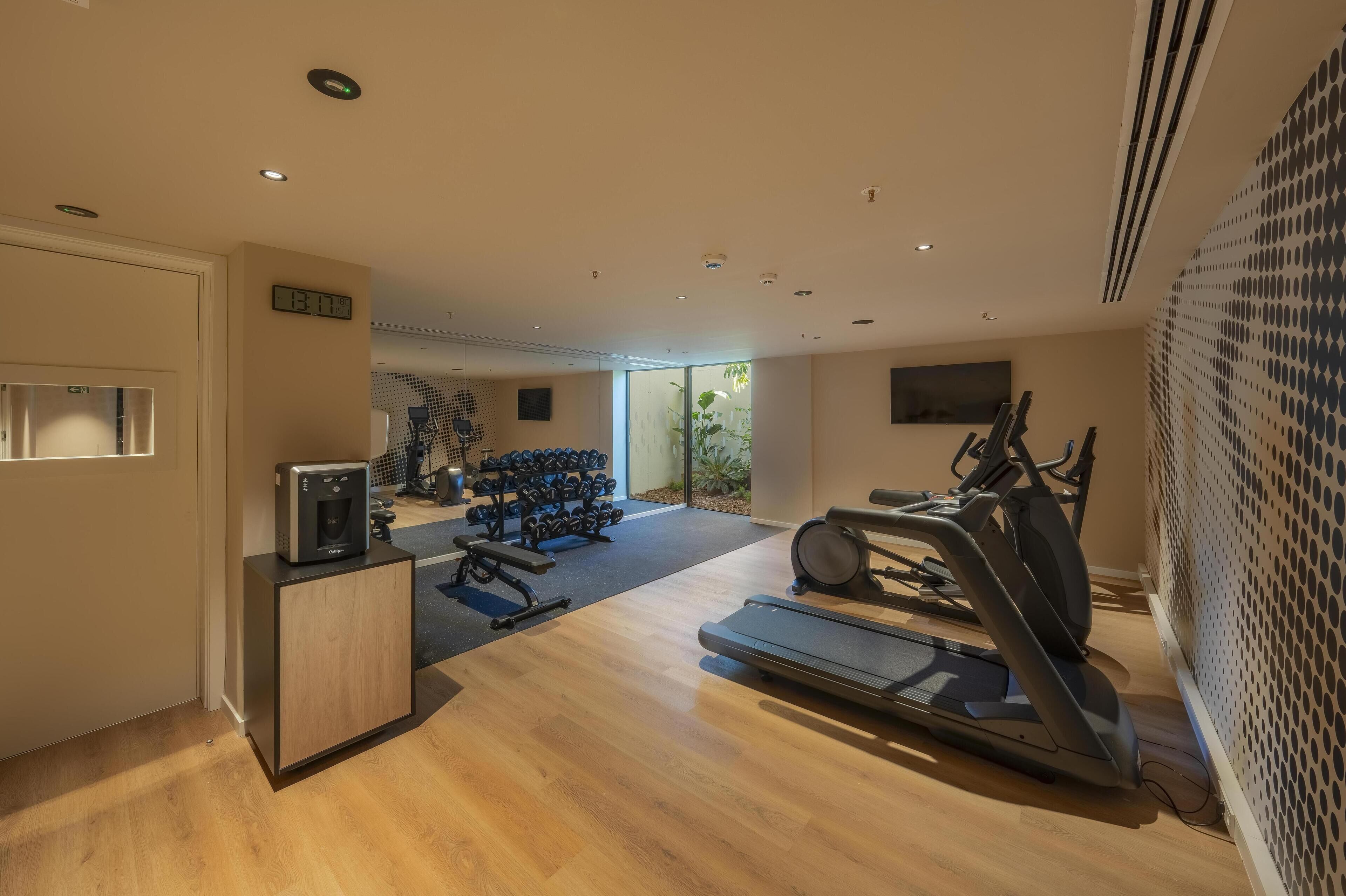 A modern gym with a treadmill, elliptical, and dumbbells.