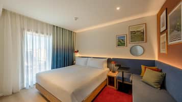 A hotel room with a large bed, a sofa, a small table, and a wall-mounted round mirror.