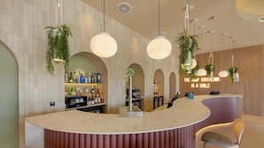 A modern bar area with a curved counter, multiple hanging light fixtures, and a bar stocked with bottles. - Hampton By Hilton Alicante Airport (Elche)