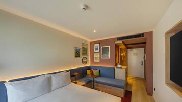 A hotel room with a bed, a sofa, a small table, and a door leading to a hallway.