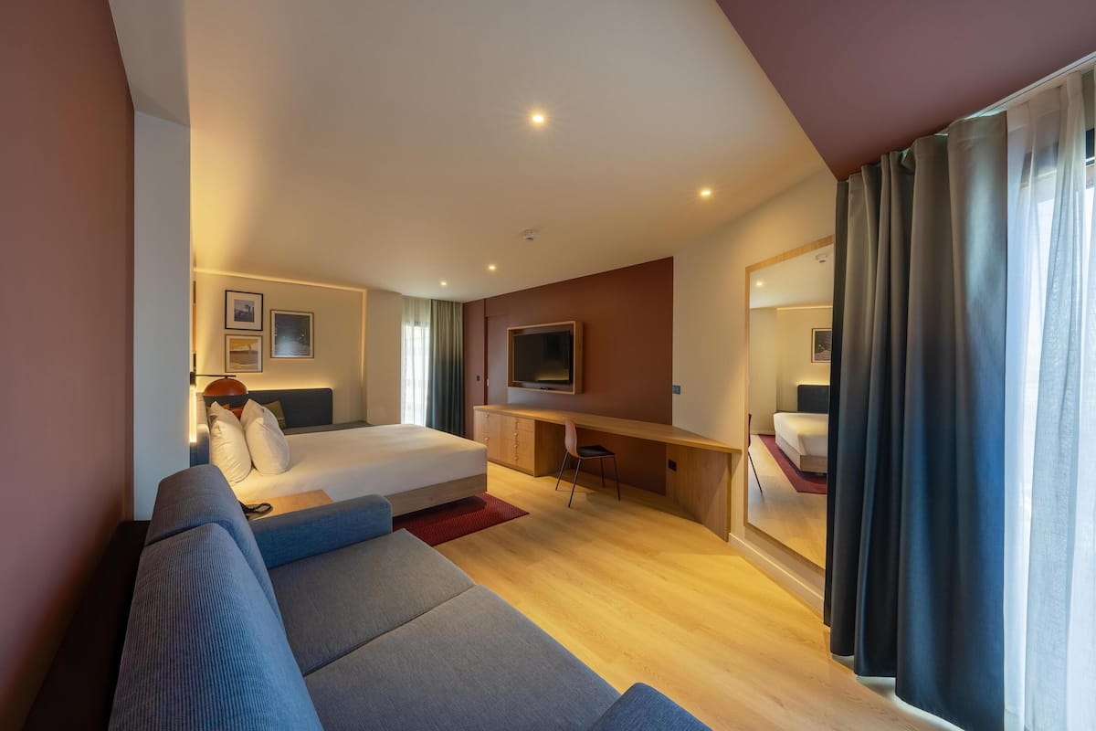 Quarto de hotel moderno com cama, sofá, escrivaninha e televisão.