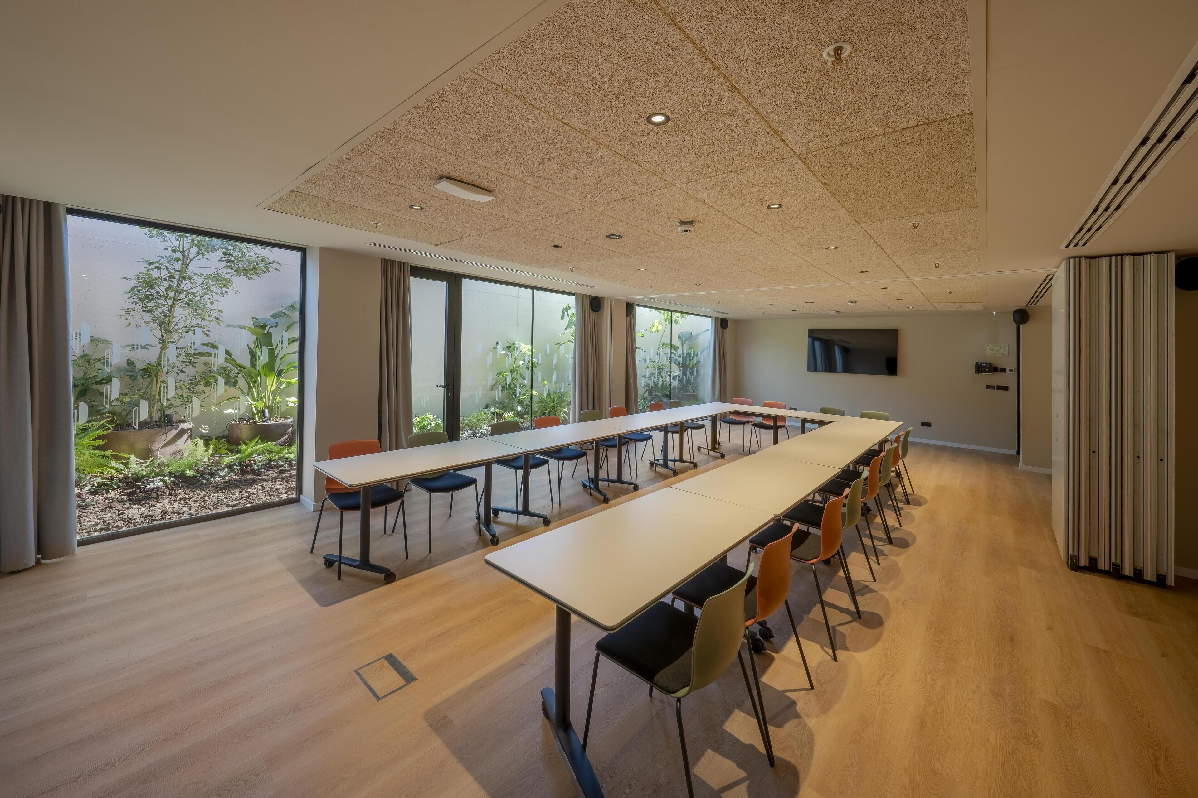 A conference room with a long table, chairs, and large windows with a view of greenery.