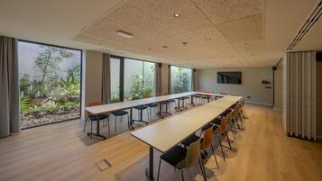 A conference room with a long table, chairs, and large windows with a view of greenery.
